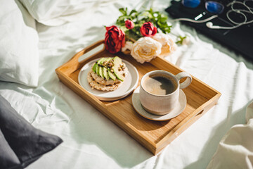 Tray with cup of coffee and light sandwich in a bed with Laptop on the background, morning light