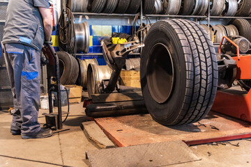 Obraz na płótnie Canvas Tire workshop operator who uses a machine to mount or remove a truck wheel.