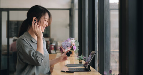 close up of asian young girl use wireless earbuds to have online language courses and searching information via laptop computer at cafe. © wichayada