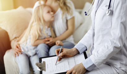 Obraz premium Doctor and patient. Pediatrician using clipboard while examining little girl with her mother at home. Sick and unhappy child at medical exam