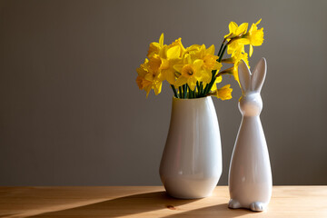 Narzissen in weißen Blumenvase und ein weißer Osterhase  auf einem Holztisch. Stylisches Deko zur...