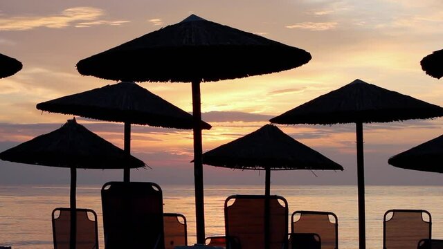 Outlines of beach umbrellas and sun beds at idyllic sunset on the beach with the sea in the background in backlight
