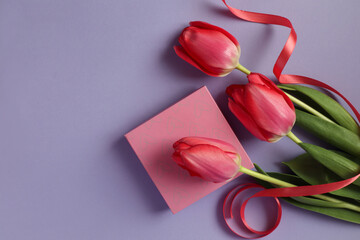 A gift with a bouquet of pink tulips and a scarlet ribbon on a pastel background, top view, space for text