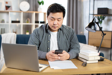 Fototapeta premium Asian male employer sitting at table and using gadgets