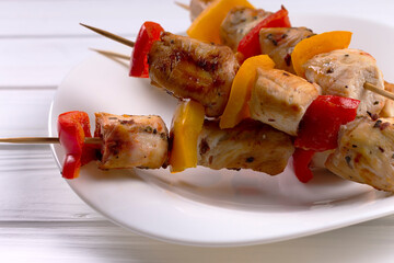 Chicken kebab with vegetables, on a white plate. Wooden background.