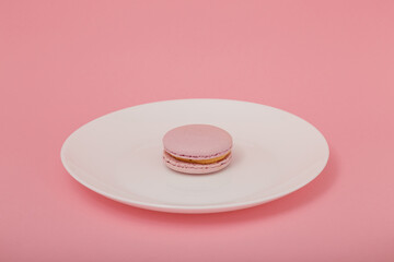 One pink macaroon on white plate on pink paper background. Sweet bakery, copy space. Overweight, diet, diabetes, healthy eating habits.