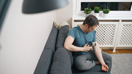 Man massaging arm with massage percussion device at home.