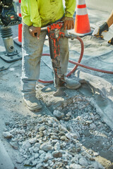 Worker on a concrete slab using a jackhammer to break up the pieces.