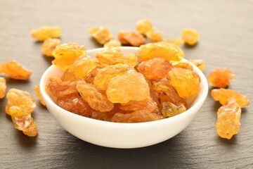 Yellow-golden organic raisins in a white saucer, close-up, on a slate board.