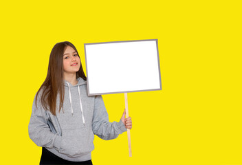Young girl holding protest blank sign board over yellow background. Mockup.