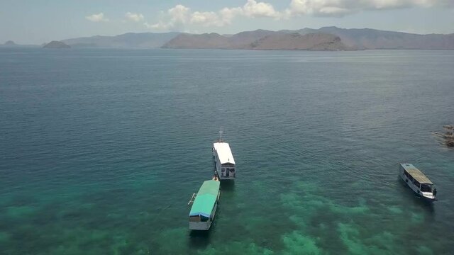 Small cruising boats on the Idyllic waters off the coast of Pink Beach in Komodo Island, Indonesia - Aerial Fly-over shot
