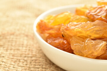 Yellow-golden organic raisins in a white saucer, close-up, on sacking.