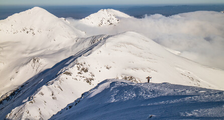 Hiker working hard and going up the mountain in snow with mountains in the background