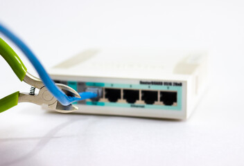 Cuts cable on router. Man cuts cord of Wi-Fi router. White router with cut cord. Side cutters cut cable on white background. Network cable in router is damaged. Hand cuts cable.