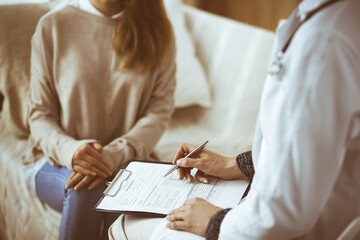 Unknown woman-doctor and patient discussing current health examination while sitting indoors. Stay...