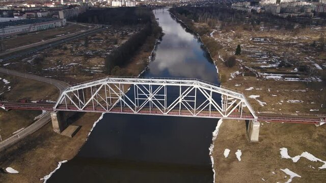 Metal railway train bridge over the river
Belarus Orsha Dnieper River. 
early spring Aerial footage from drone departing away from the bridge. downsizing landscape