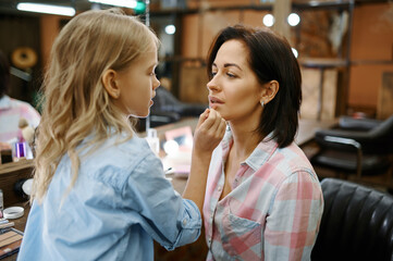 Adorable daughter paints lips to her mother, salon