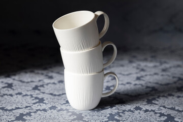 White cups on top of each other. a tower of cups on the floral kitchen table, at morning 