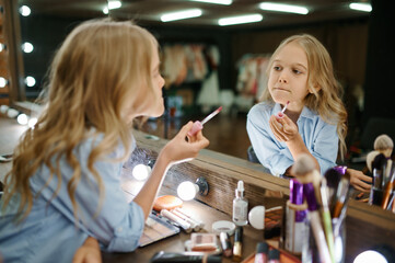 Little girl using lipstick in makeup salon