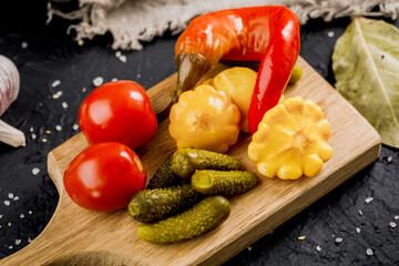 Pickled vegetables on a wooden board on a dark background. Pickles