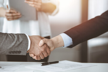 Obraz premium Business people shaking hands finishing contract signing in sunny office, close-up. Handshake and marketing