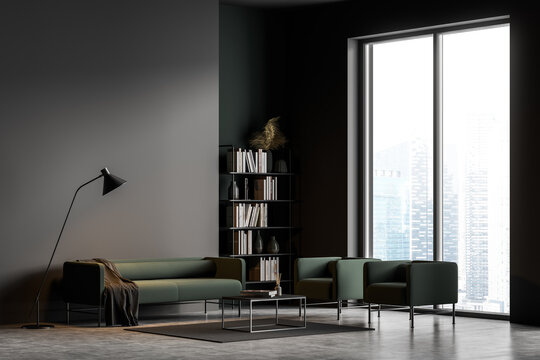 Dark grey modern living room interior with panoramic windows furnished by green sofa, armchairs, coffee table, bookshelf and lamp. Concrete floor.