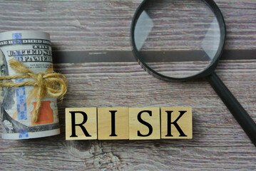Selective focus of magnify glasses, and wooden cube with word RISK. Risk management, investment, buying, and selling concept.