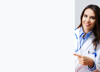 Portrait image of happy smiling female doctor pointing blank signboard with copy space empty area...