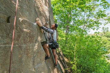 Man climber with climbing gear equipment climbs on rock wall. Canyon rocks in green forest
