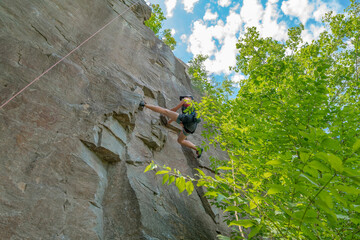 Obraz premium Woman climber with climbing gear equipment climbs on rock wall. Canyon rocks in green forest