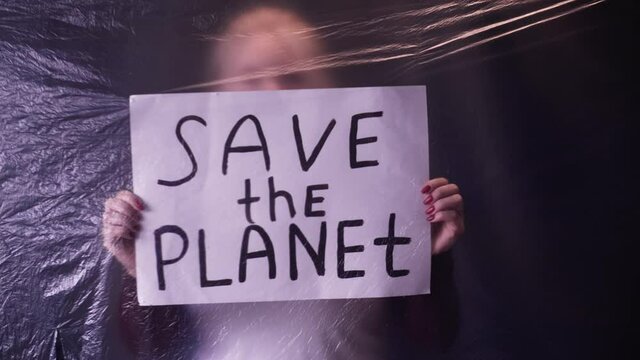 Save the planet. Earth day. Environmental strike. Defocused activist woman silhouette holding ecology inscription placard behind wrinkled texture polyethylene film on dark background.