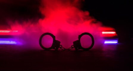 Police raid at night and you are under arrest concept. Silhouette of handcuffs with police car on...