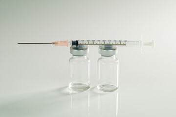 Impfen / Impfung: Eine Spritze liegt auf zwei Impf-Ampullen auf neutralen hellen Hintergrund...
