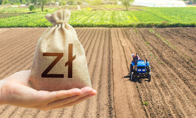 Hand with a polish zloty money bag on the background of a farm field with a tractor. Land lease,...