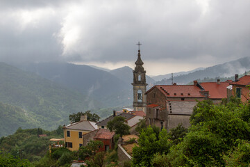 Fototapeta na wymiar The bell tower of the temple against the background of mountains, surrounded by houses with tiled roofs. Low clouds after rain.
