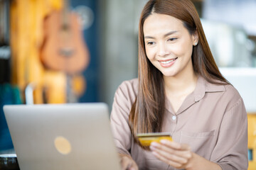 Online shopping and new normal concept.Happy attractive woman doing online shopping with credit card at home.Young girl doing e-shopping and inputting card information in laptop.