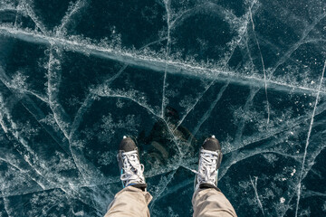 Feet in skates on the beautiful blue cracked ice of a frozen lake. View of the top