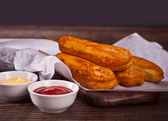 Corndogs on a stick with ketchup and mustard on the wooden table.