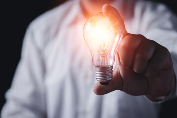 Naklejka na ściany i meble The hand of a man with a light bulb. The idea of ​​inspiration from online technology.innovation idea concept.