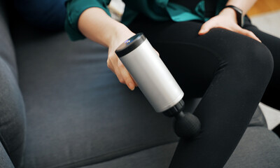 Woman massaging leg with massage percussion device at home.