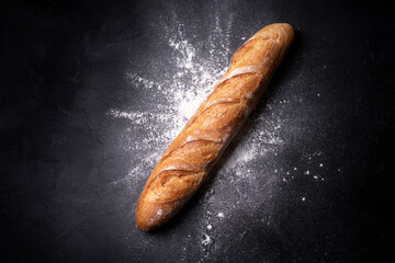Crispy french baguette in splashes of wheat flour on a black background. - obrazy, fototapety, plakaty