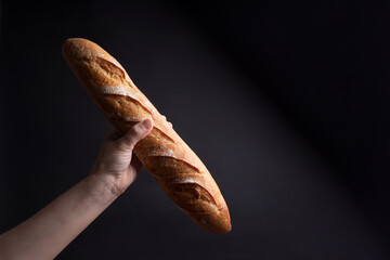 Female hand holding a crispy French baguette on a black background