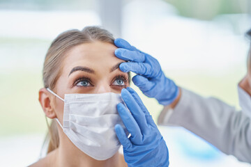 Eye-doctor in mask checking up on female patient