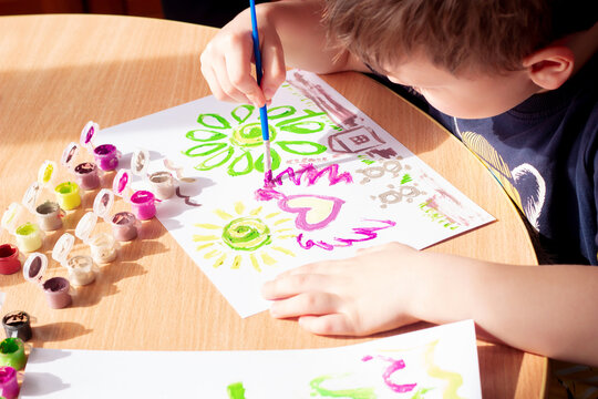 The child is drawing heart, flower, sun, bears, house with bright colors on white sheets 