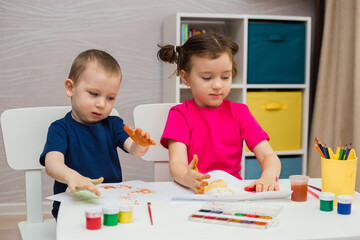 little girl and a boy sit at a table with and draw with their palms on paper