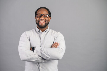 Concept of confident and stylish person. Full length of cheerful young african man keeping arms crossed and looking at camera while standing against grey background, smiling widely and sincerely