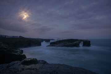 Full moon just before sunrise over the iconic arch of As Catedrais beach