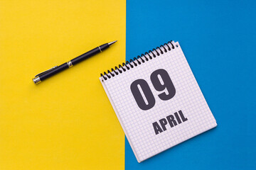 April 9th. Day of 9 month, calendar date. A notebook with a spiral and a pen lies on a yellow-blue background, flat lay, copy space