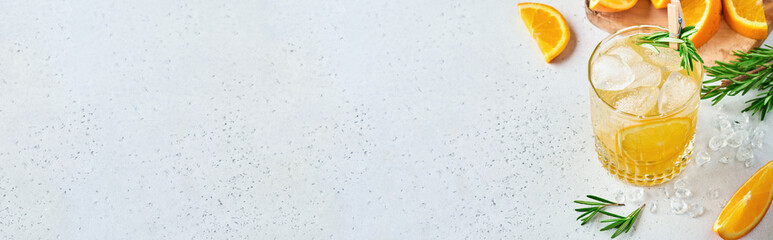 Orange juice or cocktail with rosemary and orange with ice in glass, cold summer lemonade on light gray slate, stone or concrete background. Beach concept with deep sun shadow. Top view.