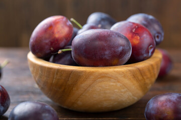 Fototapeta na wymiar Fresh plums in a wooden bowl on a brown table.